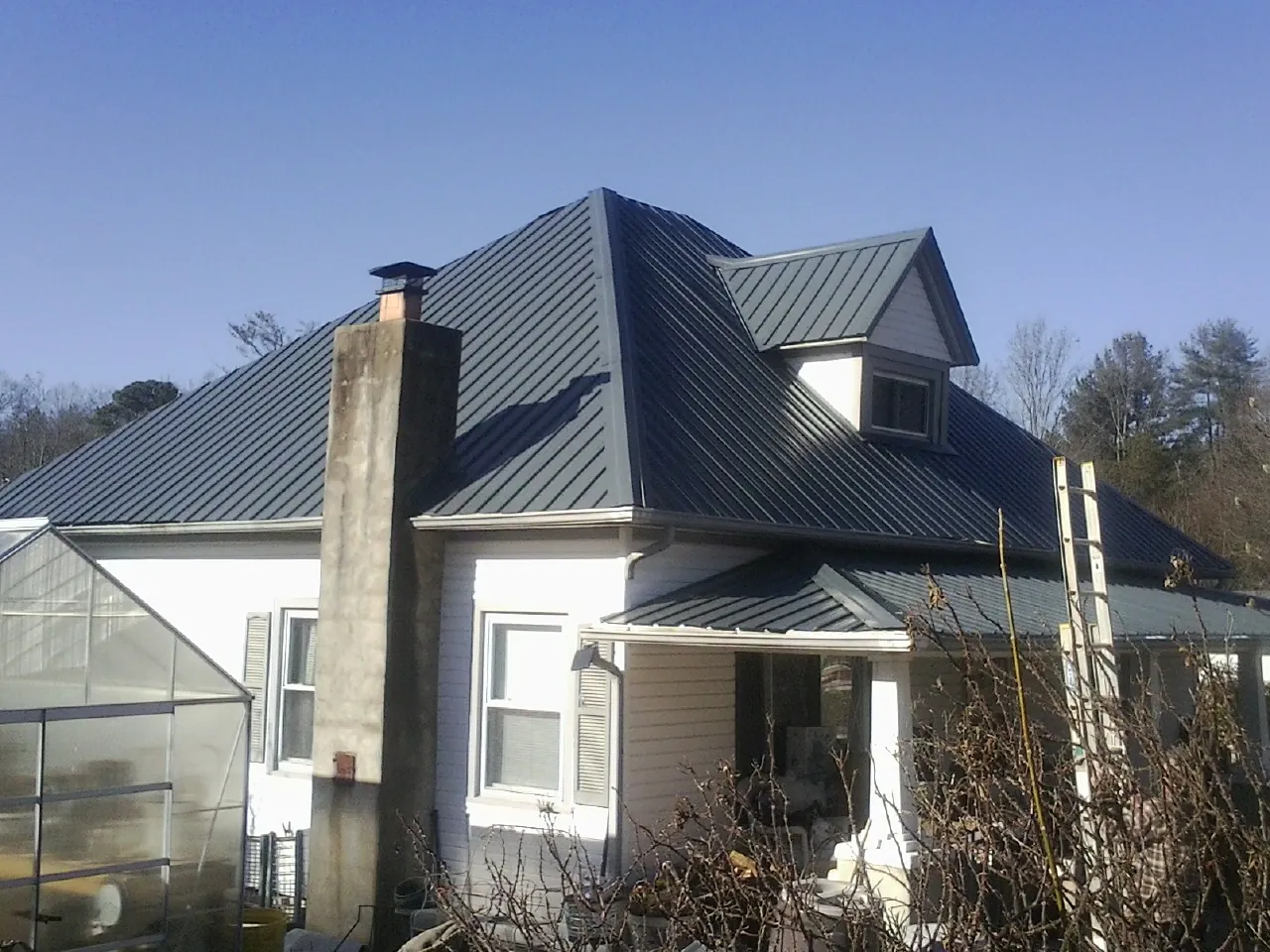Dark blue standing seam metal roof on a white farmhouse with dormer — Slate & Tile Roof Repair by Roofing Brothers in Solon