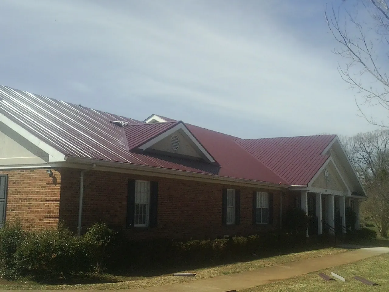 Red metal roof with gabled entries on a long brick building, from a Hail Damage Roof Repair job in Solon