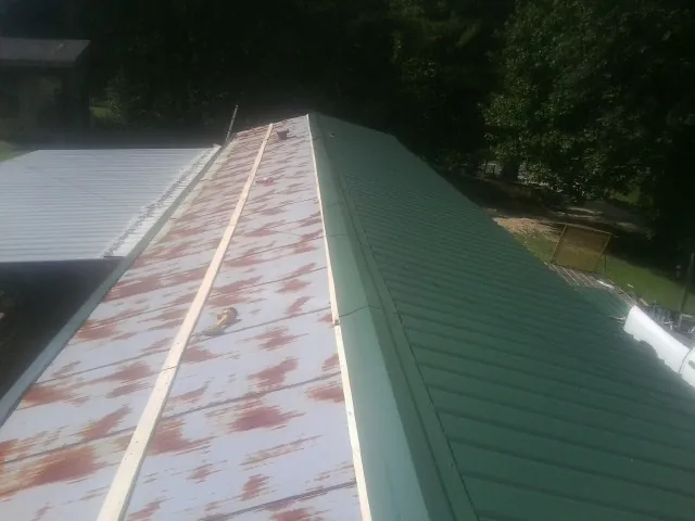 Old rusted panels beside newly installed green metal roofing — Wind Damage Roof Repair by Roofing Brothers in Solon