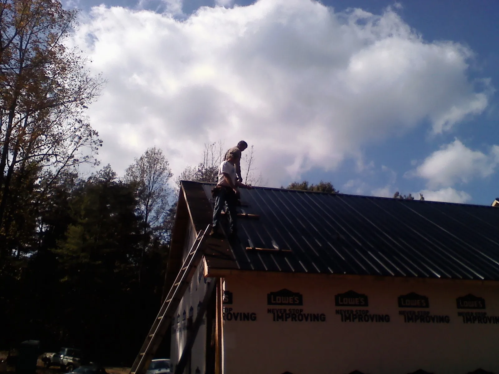 Roofer fastening dark metal panels high against a cloudy sky, from a Roof Inspection job in Solon
