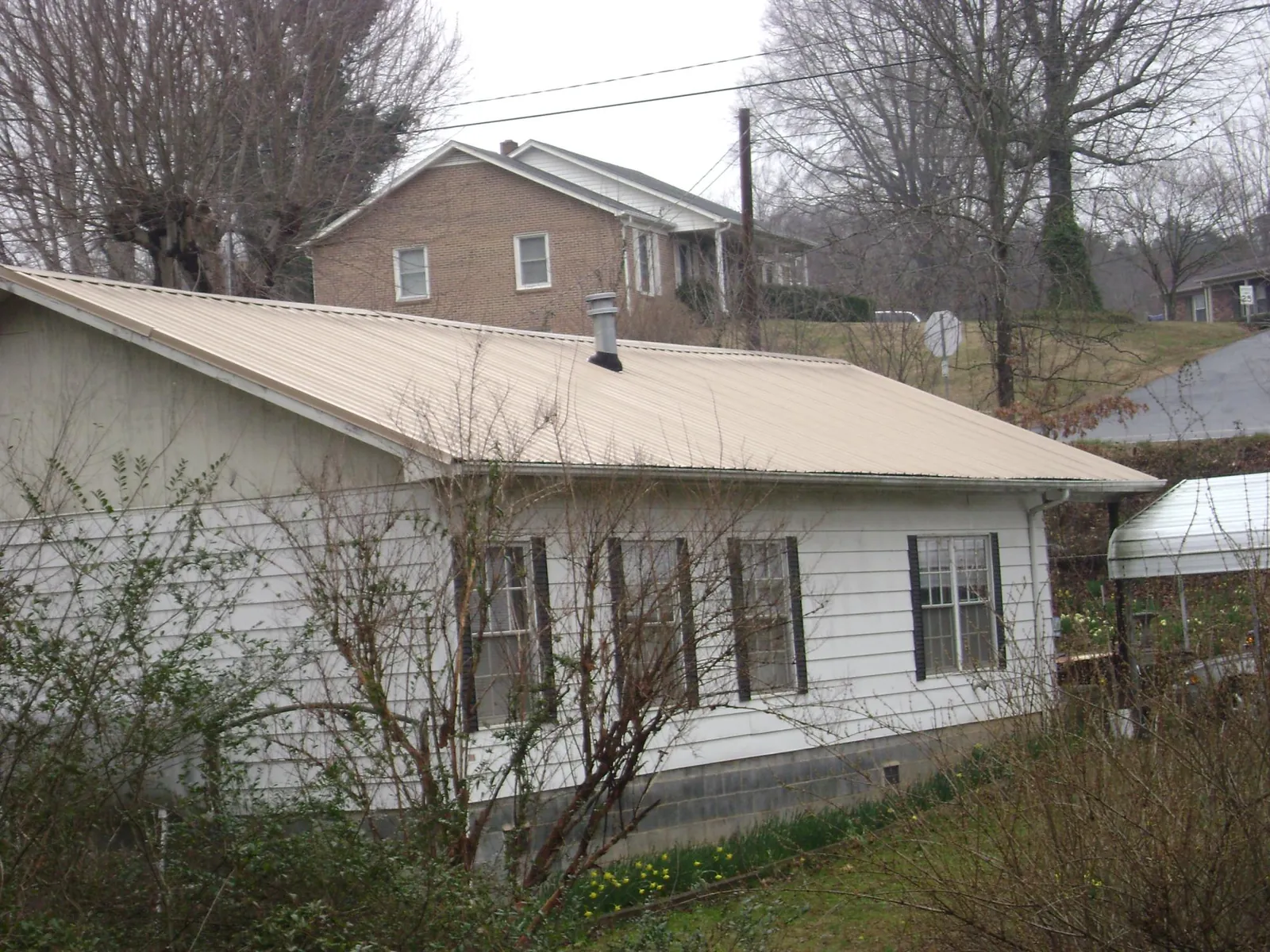 Tan metal roof on a white sided house set into a hillside — Commercial Roofing by Roofing Brothers in Solon